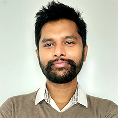 Portrait of man with short dark hair and a beard wearing collared shirt under sweater