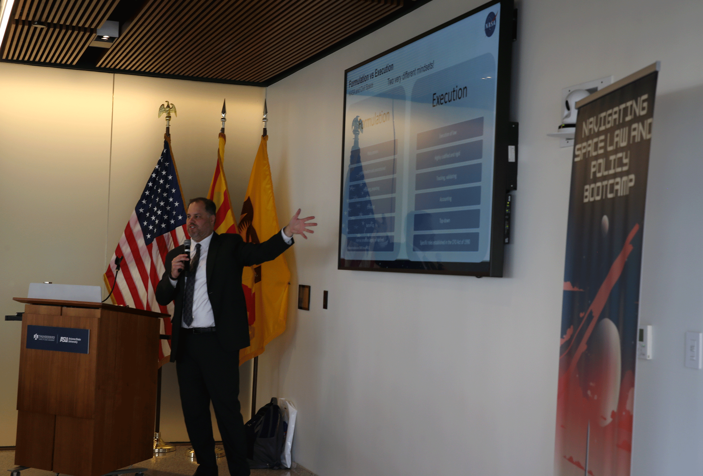 A man gestures at a screen while speaking into a mic