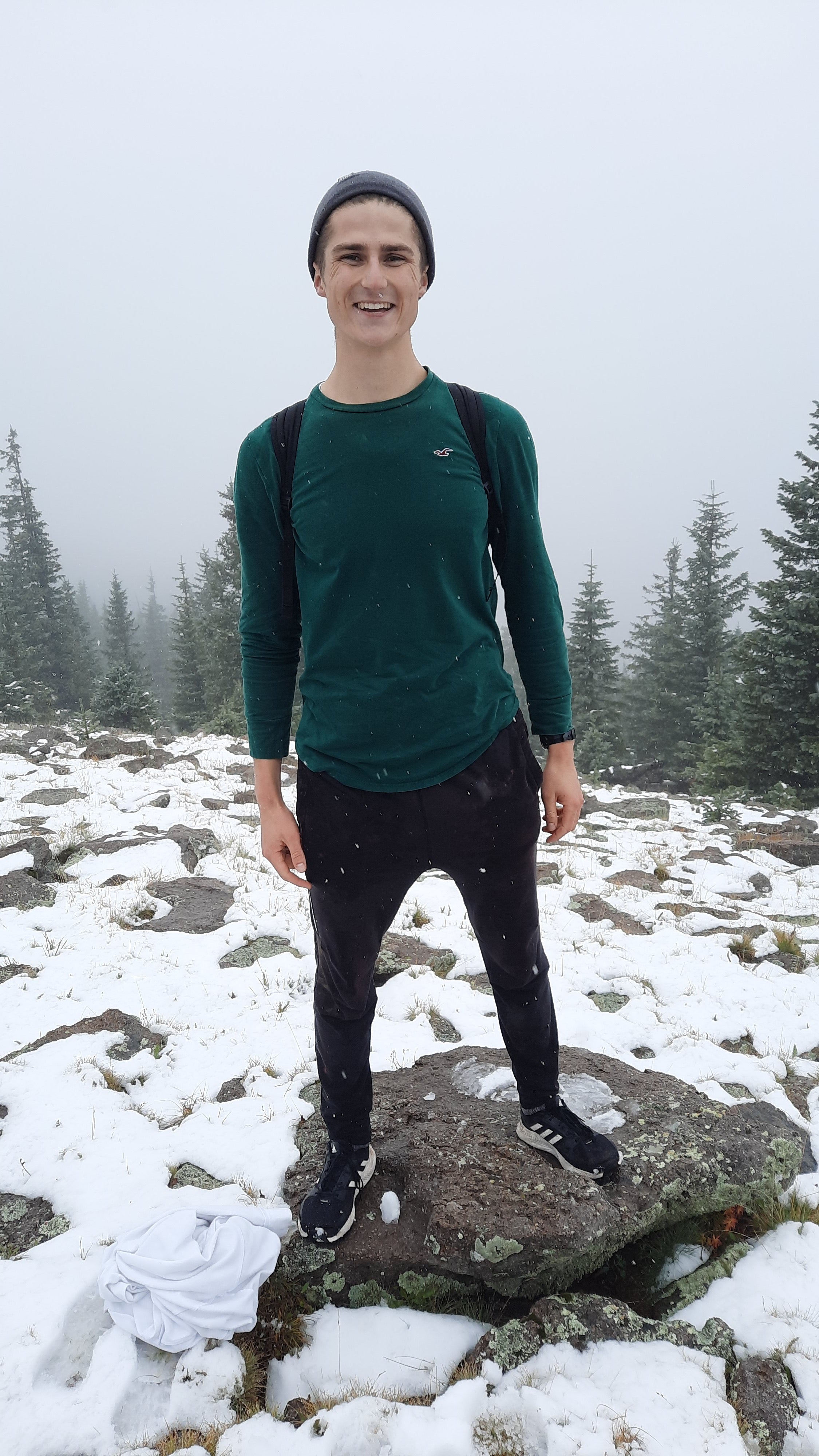 ASU student Spencer Jensen smiling and standing on a rock in a snowy, outdoor setting.