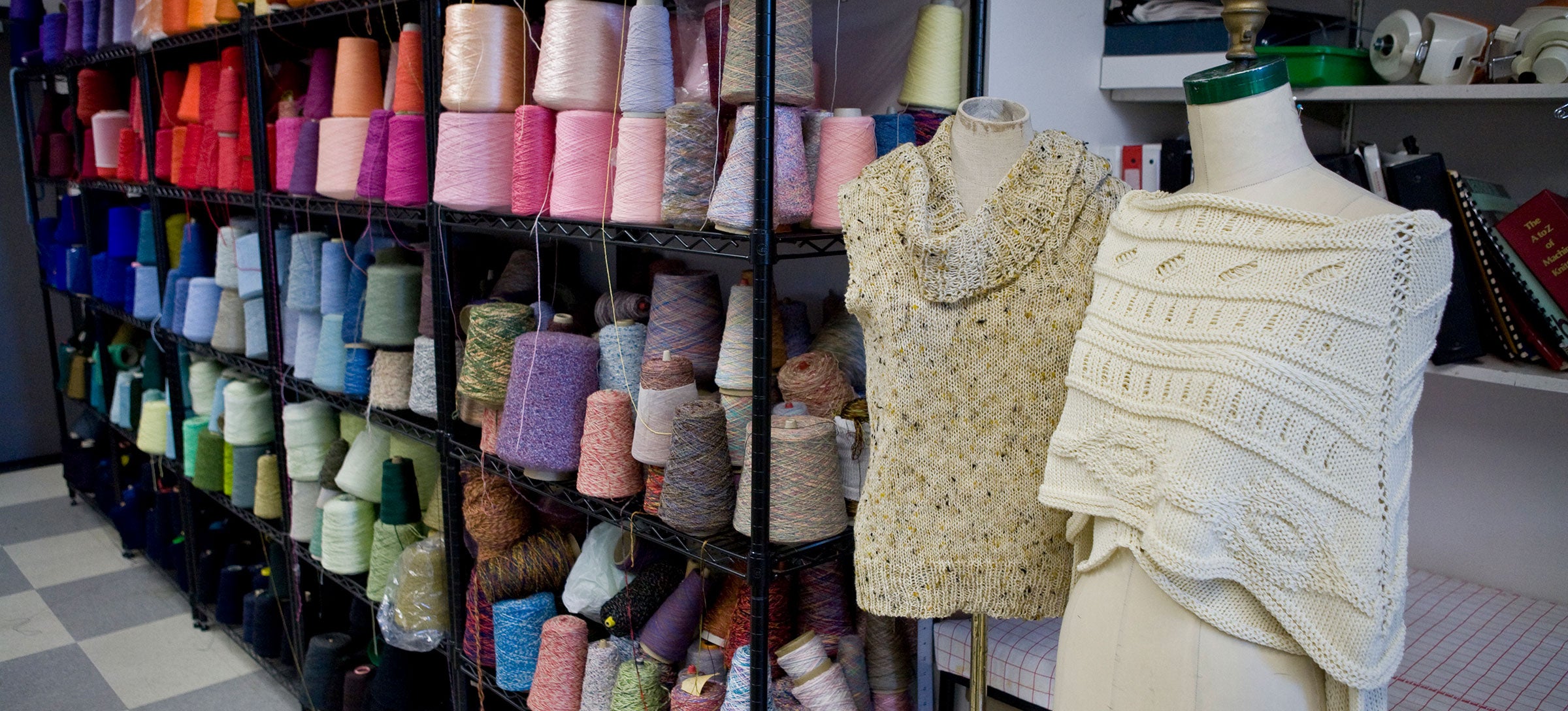 Bookshelves full of cones of thread stand behind mannequins holding knitwear