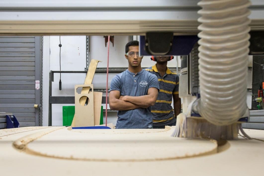 A man watches a computerized ShopBot cut out pieces of wood