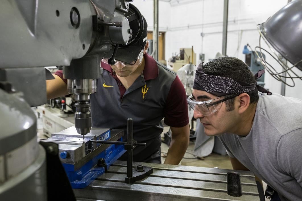 Two men work with a drill bit.