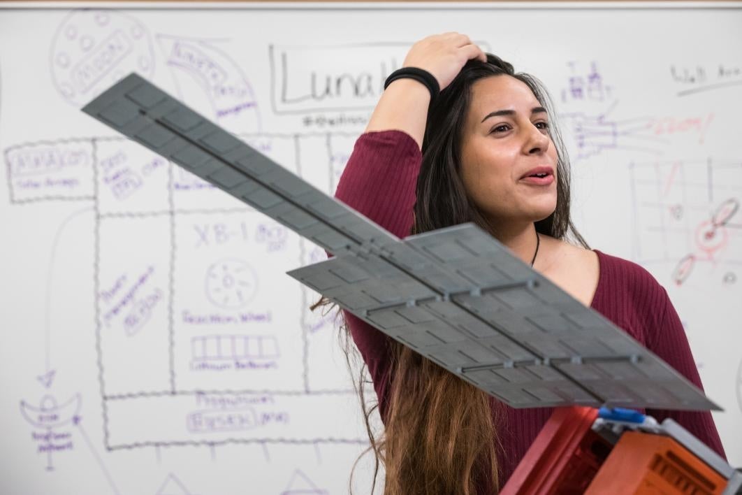 A woman discusses a satellite space mission in front of a whiteboard