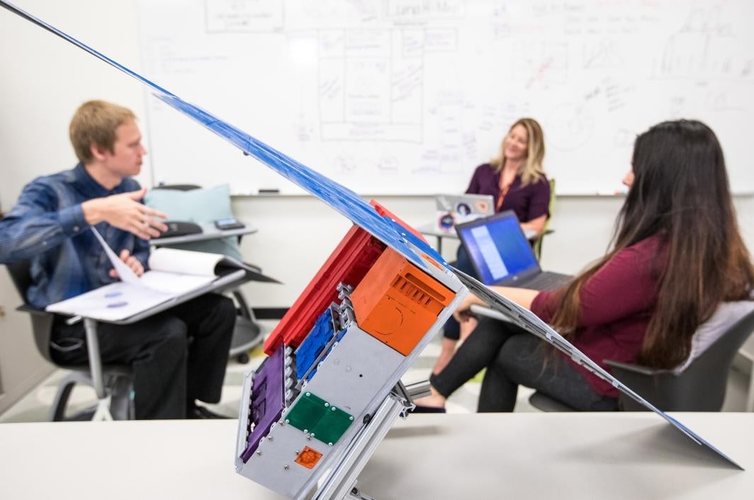 A team sits in front of a whiteboard with a satellite model in front of them