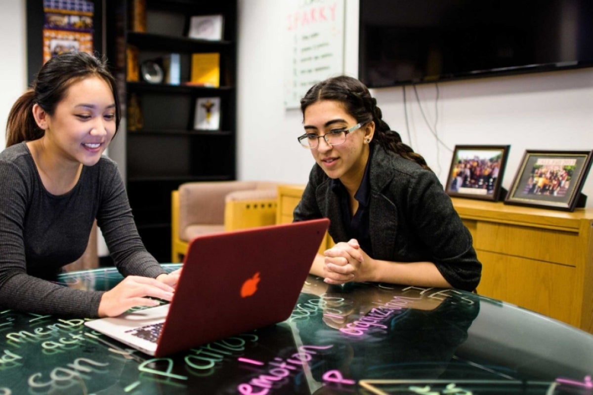 Two women sit at a table and look at a laptop