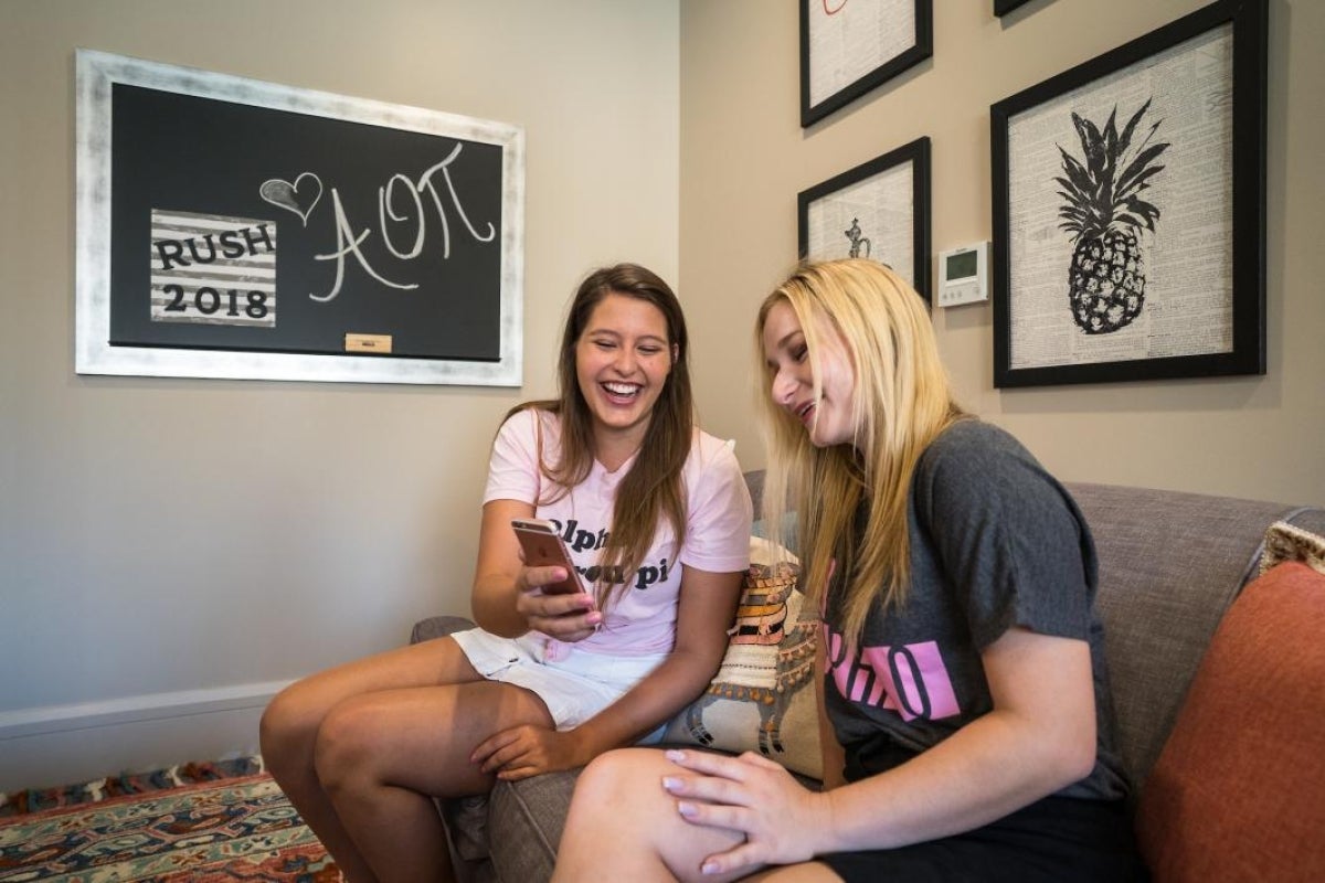 two women sitting on couch, looking at cell phone