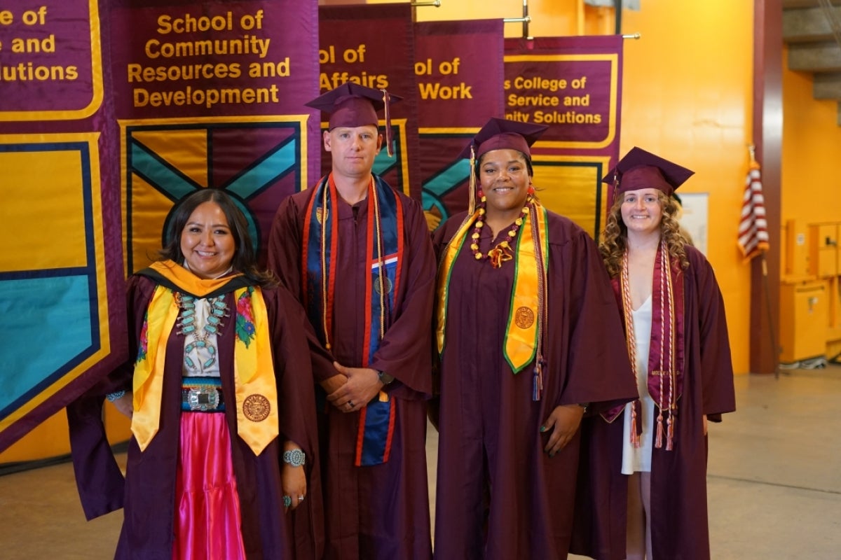 Graduates stand posing for a photo in their graduation gowns, caps and stoles.