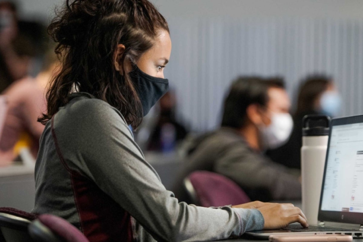 Woman wearing a mask in a classroom while using a laptop