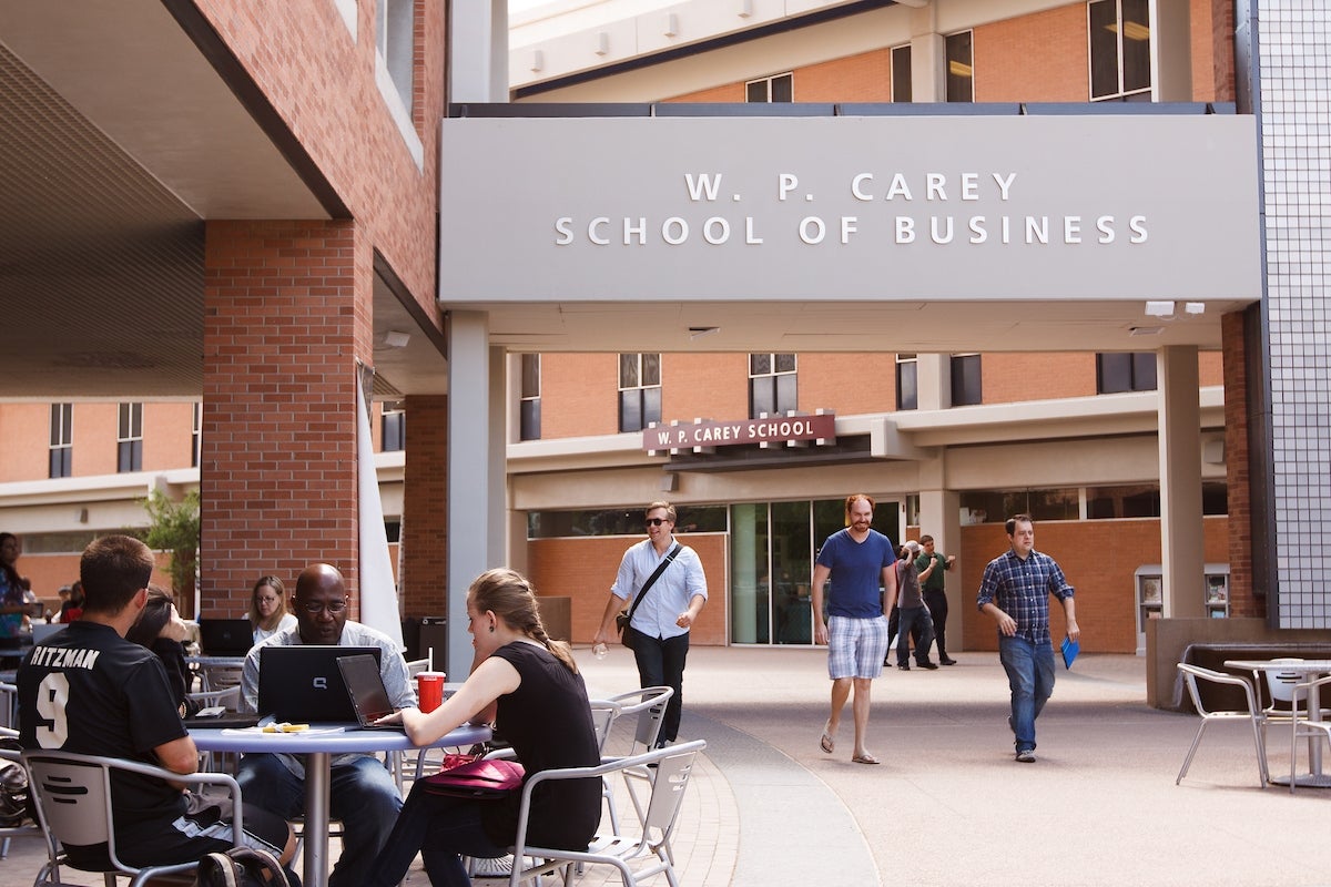 students and professors sit and walk around the exterior of the W. P. Carey School of Business building on ASU's Tempe campus