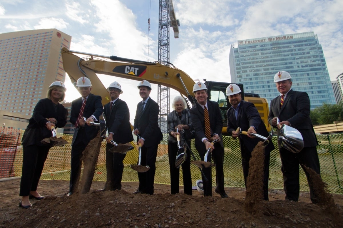 A row of people turn over shovels of dirt at a groundbreaking