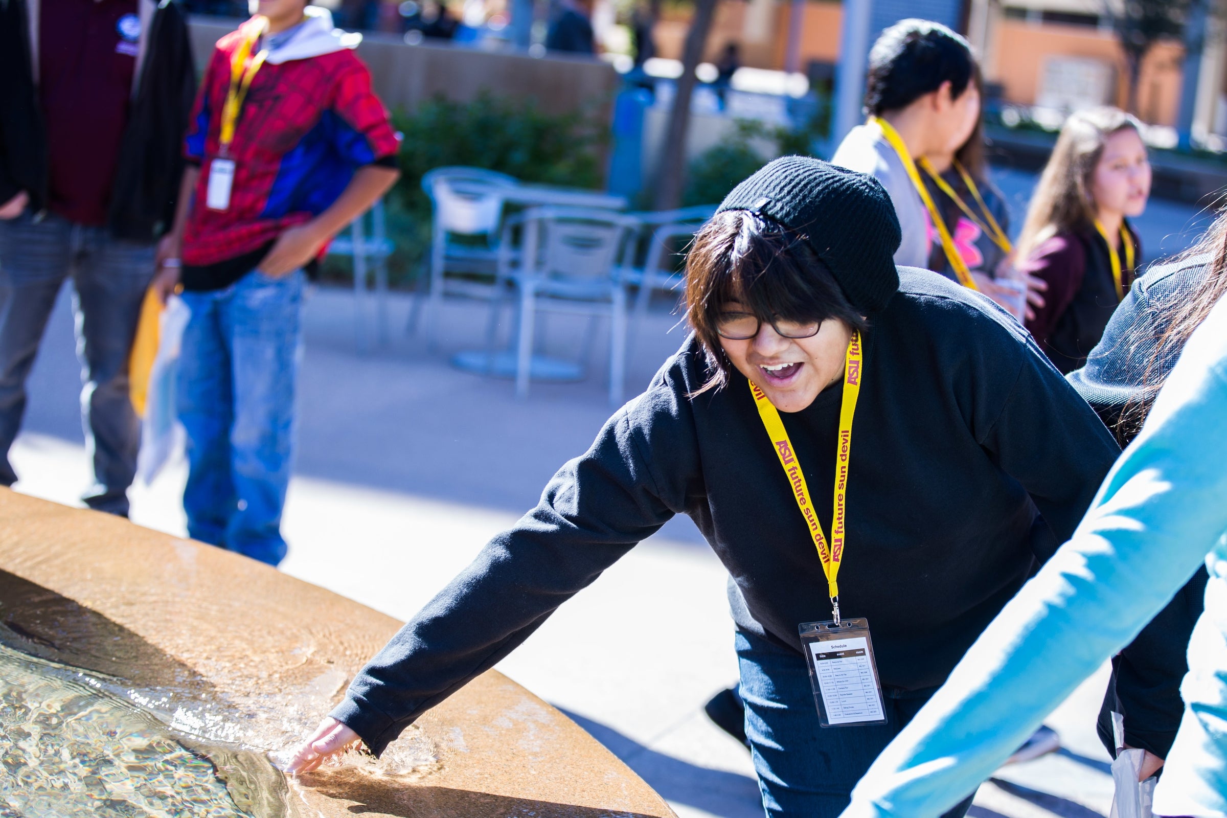 A high schooler splashes his hand in a fountain