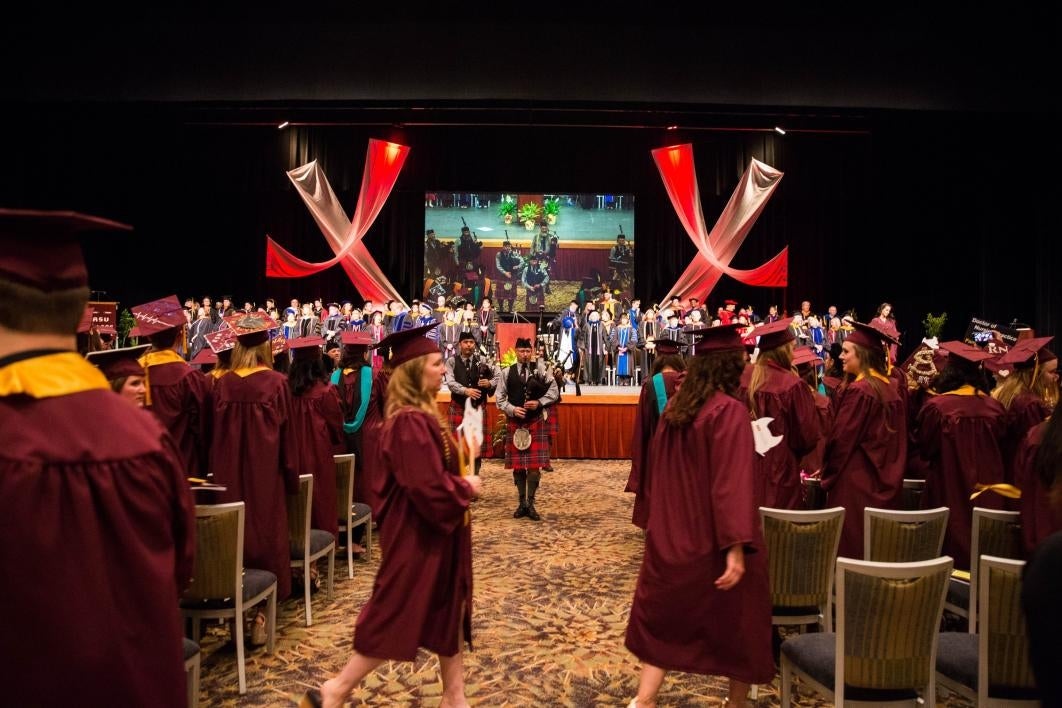 students finding seats while bagpipers play