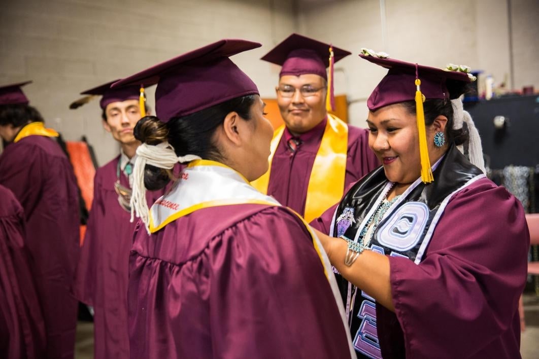 graduate helping friend adjust regalia