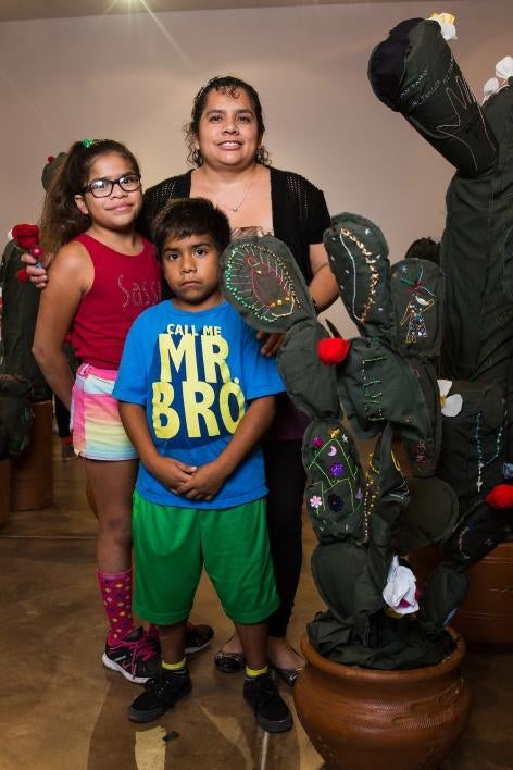 A family poses with a cloth cactus embroidered with their immigration story.