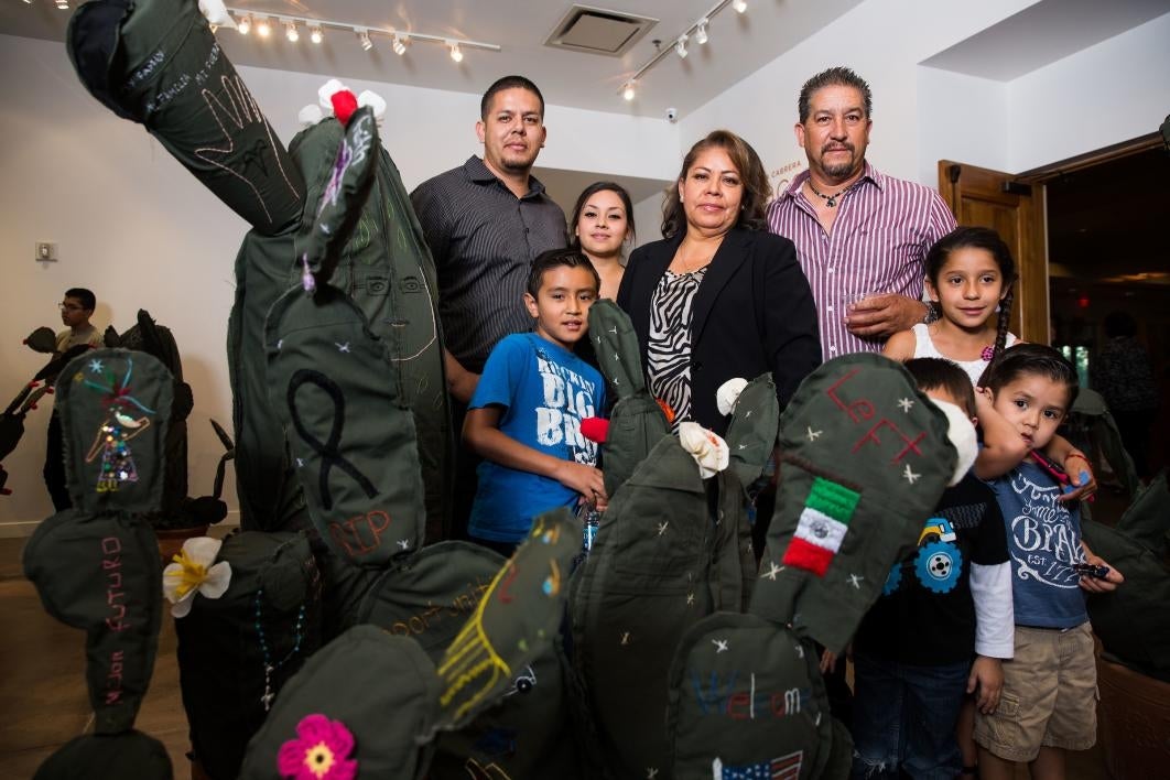 A family poses with a cloth cactus embroidered with their immigration story.