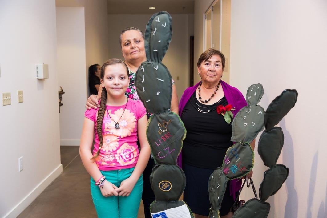 A family poses with a cloth cactus embroidered with their immigration story.