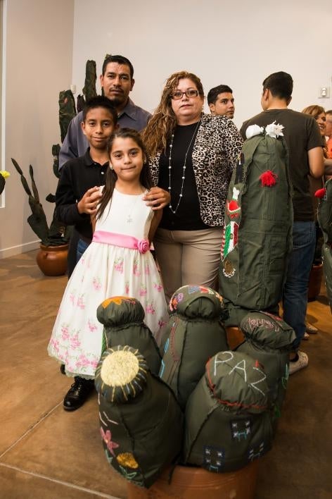 A family poses with a cloth cactus embroidered with their immigration story.