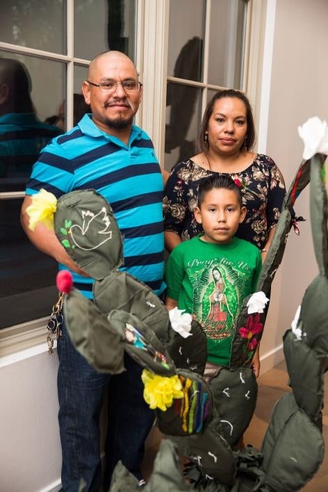 A family poses with a cloth cactus embroidered with their immigration story.