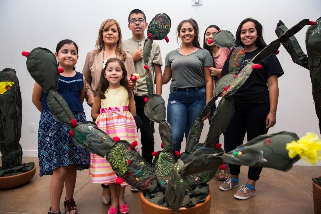 A family poses with a cloth cactus embroidered with their immigration story.