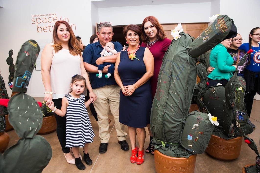 A family poses with a cloth cactus embroidered with their immigration story.