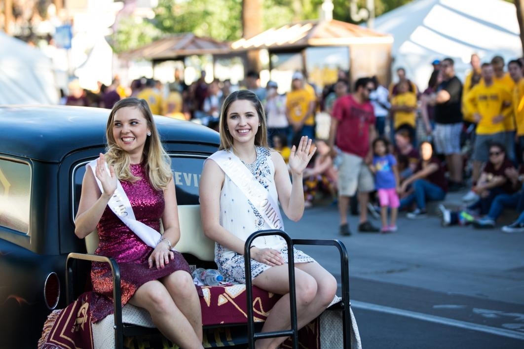 two women riding on car in parade