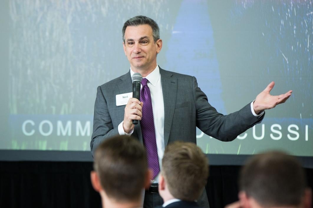 A man speaks in front of a projector screen