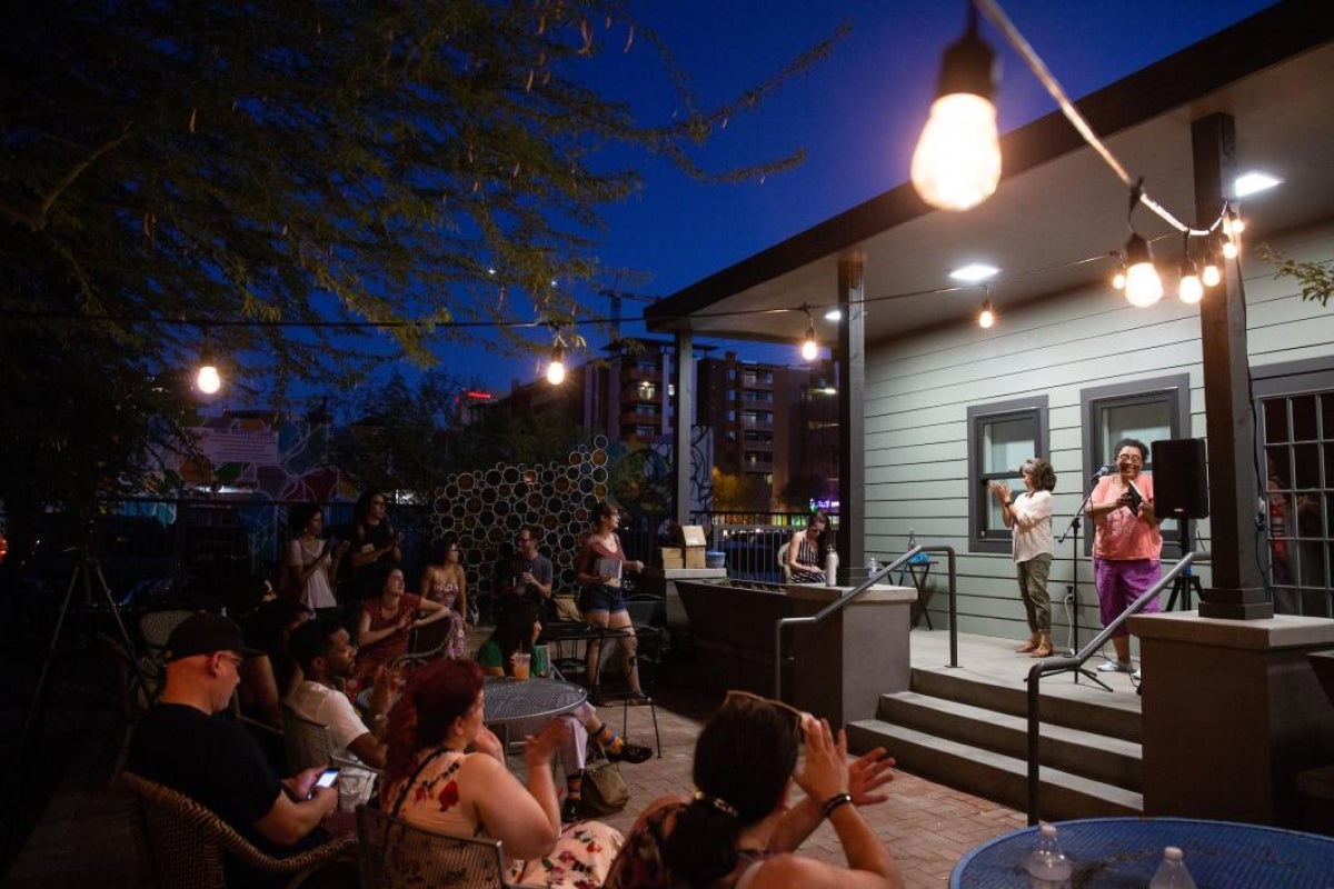 crowd listening to poetry reading on a patio outside a house at night