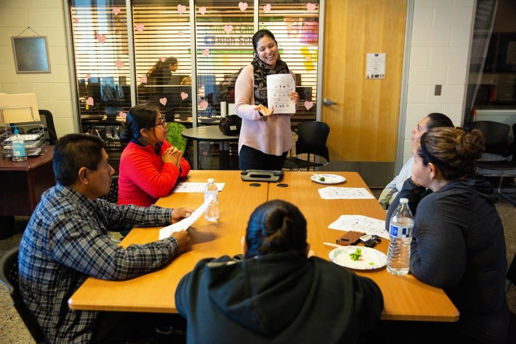 woman standing holding a paper as she talks to adults sitting around a table