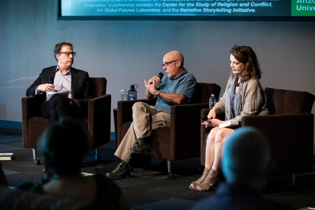 three people seated on a stage with microphones