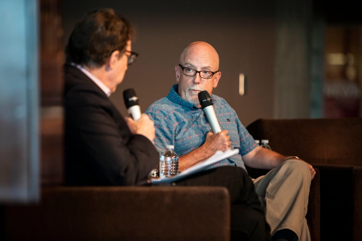 two men seated on a stage with microphones