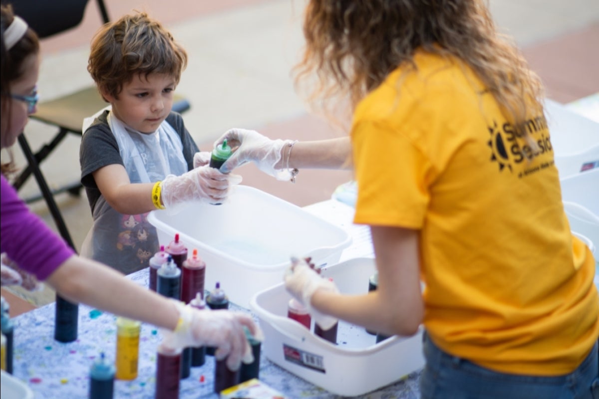 young boy wearing an apron learns how to tie-dye a shirt