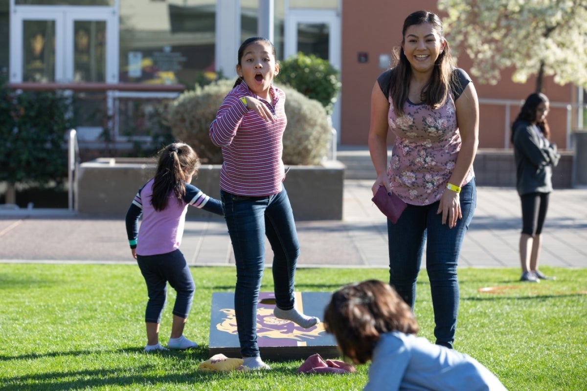 two girls have excited expressions as they play corn hole