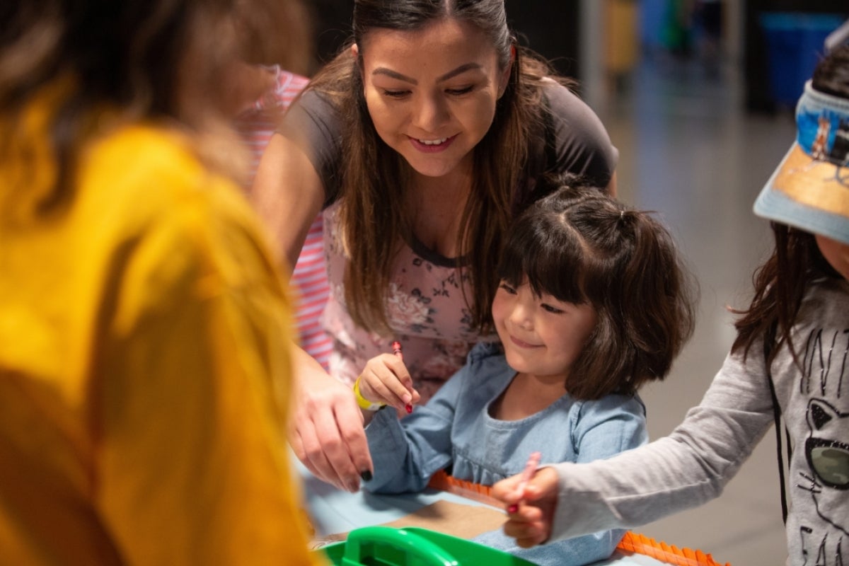 teenage girl helps a small child make a paper puppet