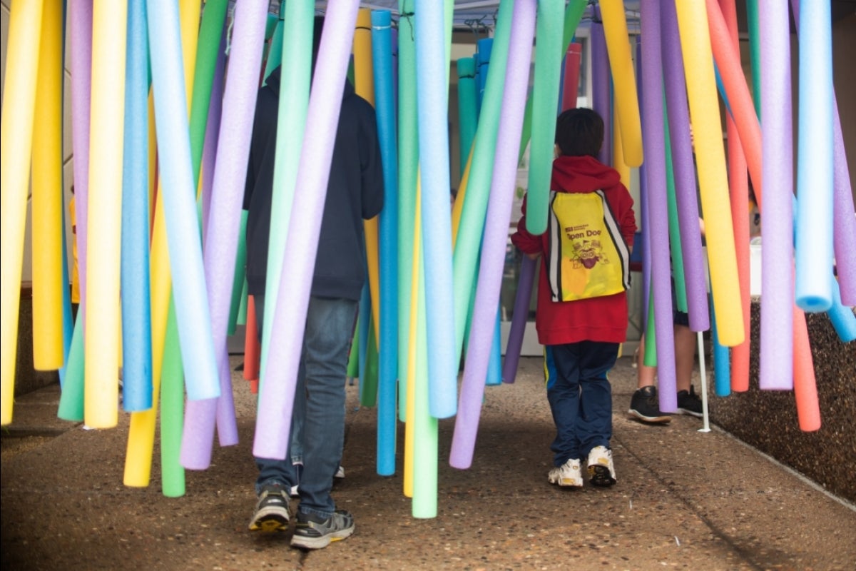 people walking through hanging pool noodles