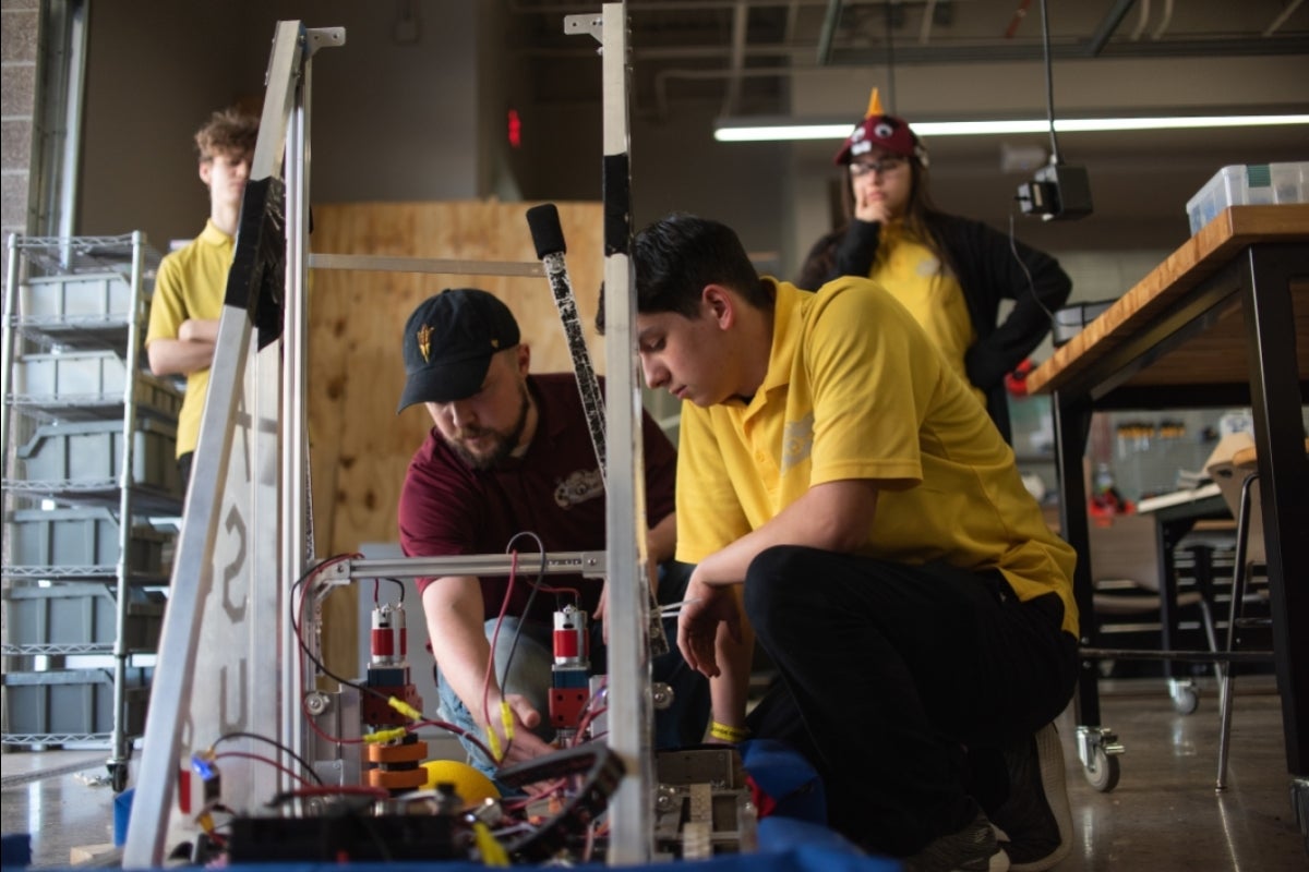 two men kneel down to work on a robot apparatus