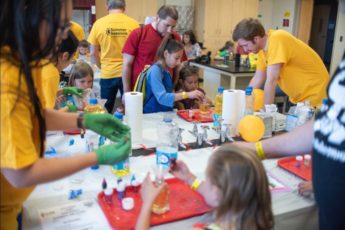 multiple children and volunteers doing science experiments around tables