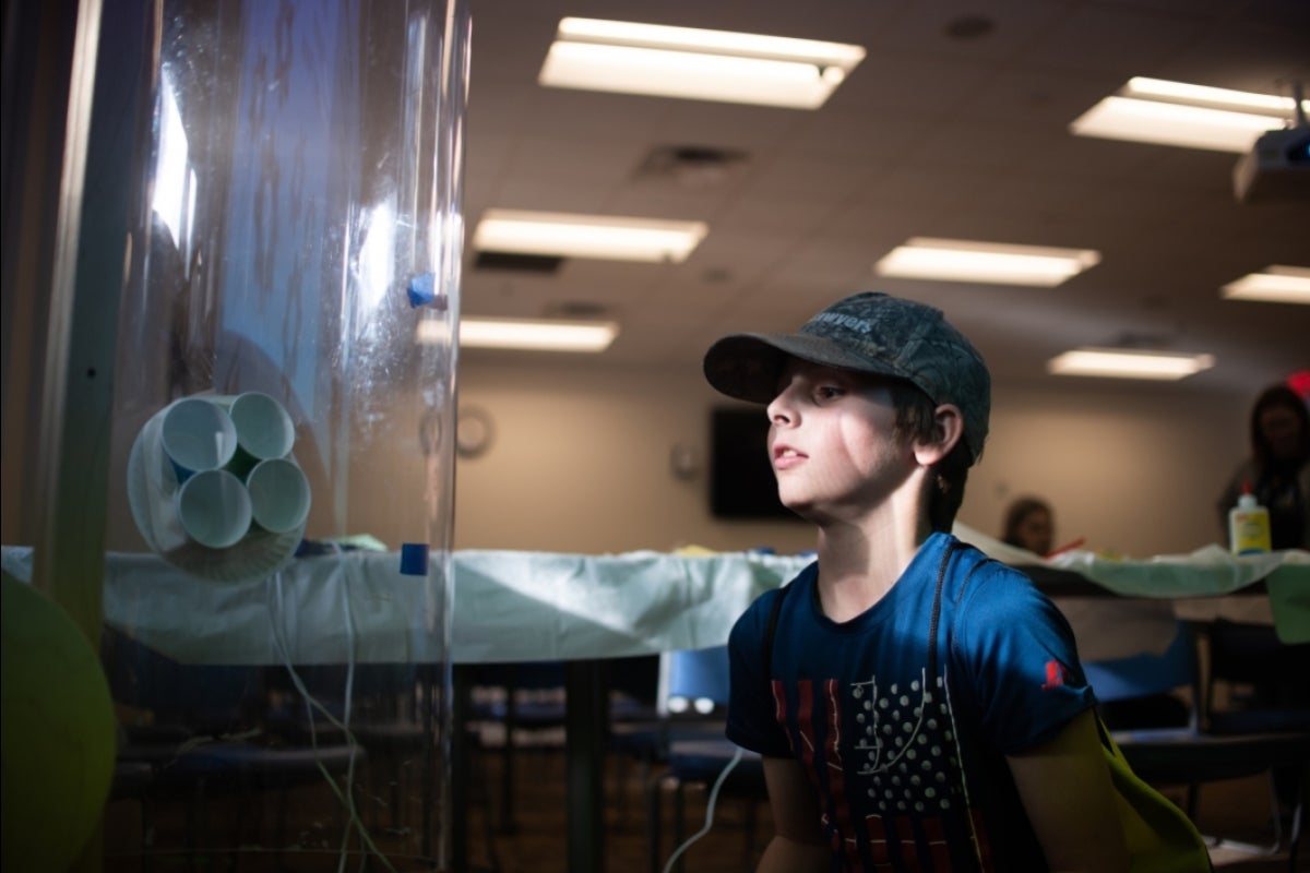 boy in a baseball cap watches his project in an air tunnel