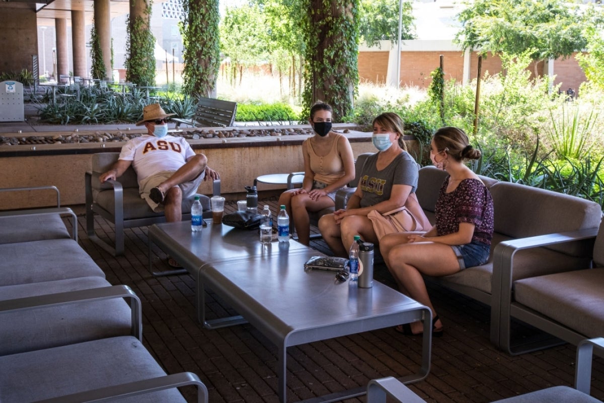 family sitting around outdoor lounge area wearing facial coverings