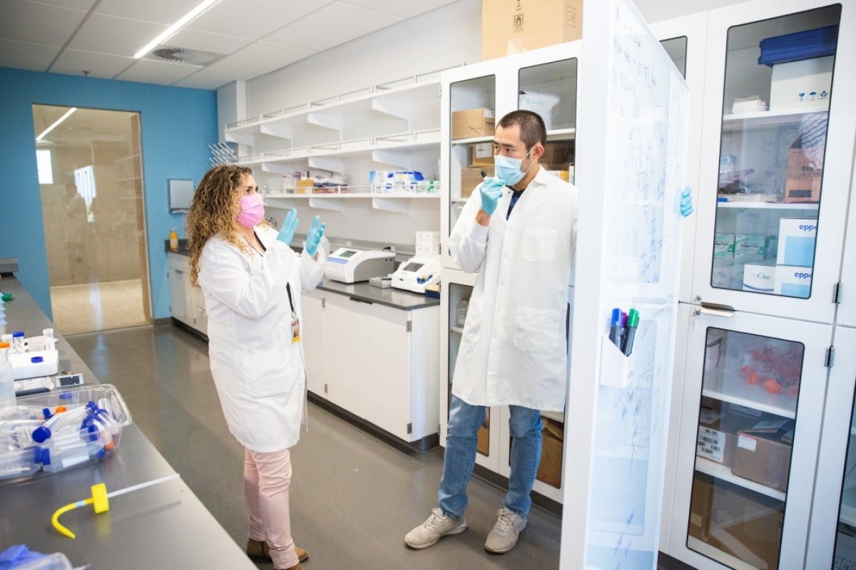 A woman and a man in lab coats discuss items on a white board in a lab