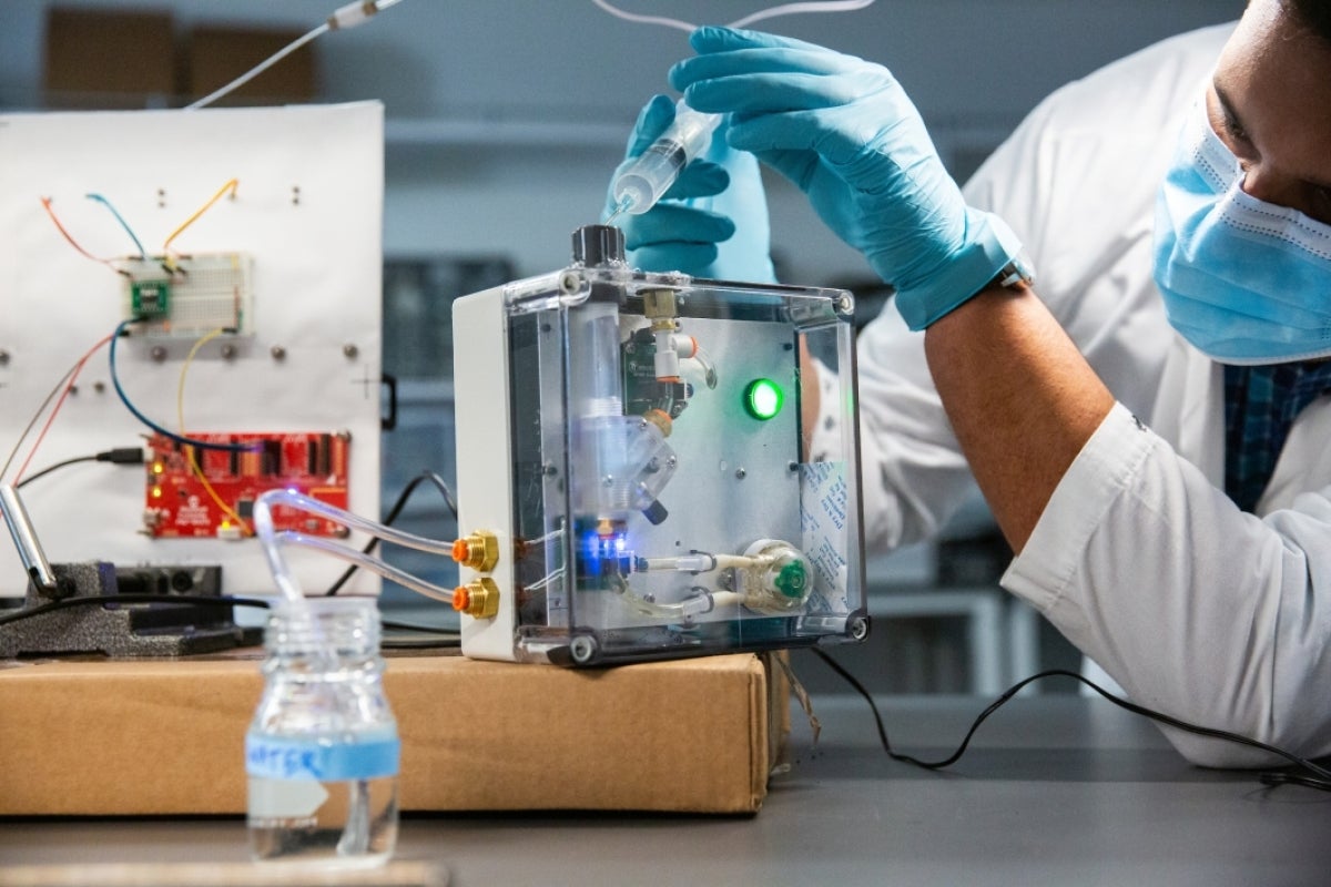 A researcher squeezes liquid from a syringe into a box containing various gauges and tubes