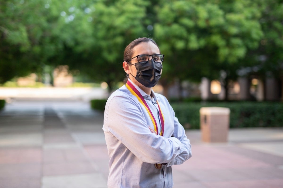 man wearing a mask and glasses poses for a portrait with his arms crossed