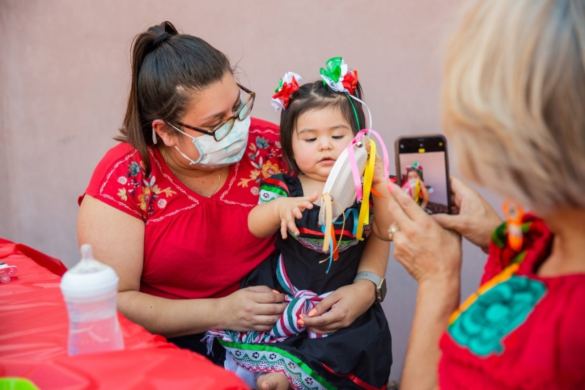 A woman holds a toddler making a Mexican Independence Day paper craft