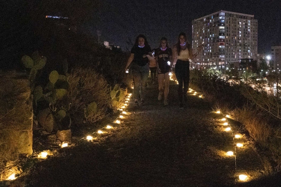 Three women wearing glow necklaces walk up the light-lined trail on A Mountain