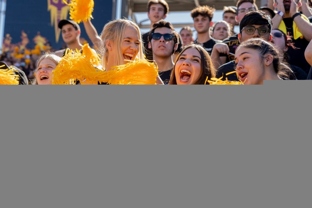 Three women cheer with gold pompoms at the ASU football game