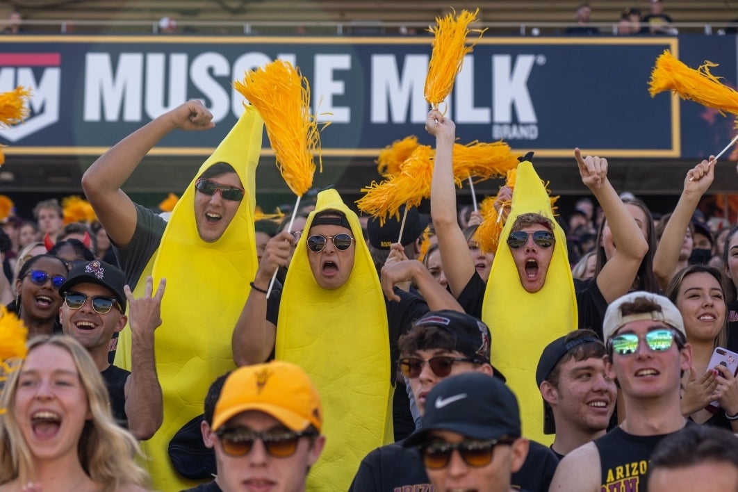 Three men wearing banana costumes cheer in the student section at an ASU football game