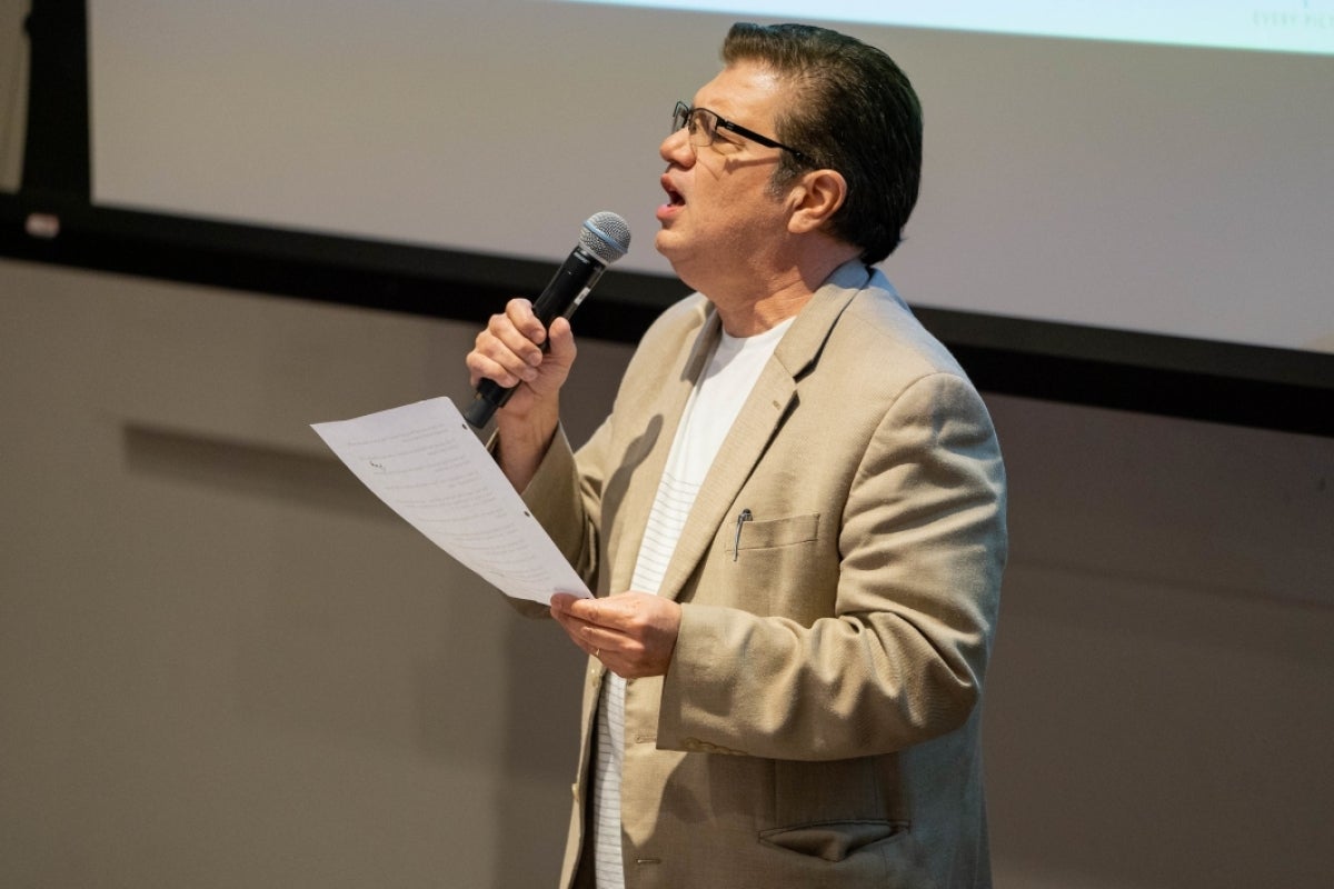 man holding a peice of paper and speaking into a microphone