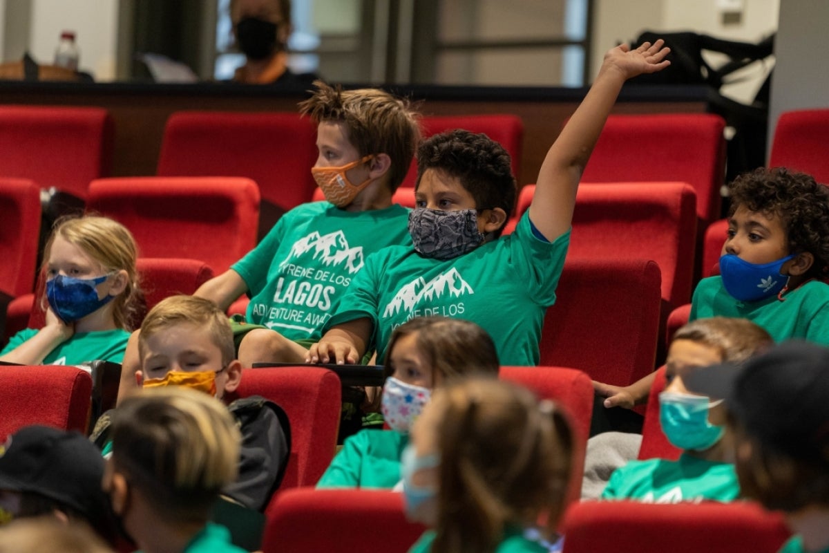 young student seated in an auditorium with his hand raised in the air