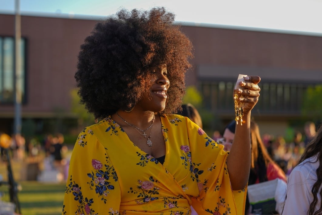 Woman in a yellow shirt with flowers on it admires a pair of earrings.