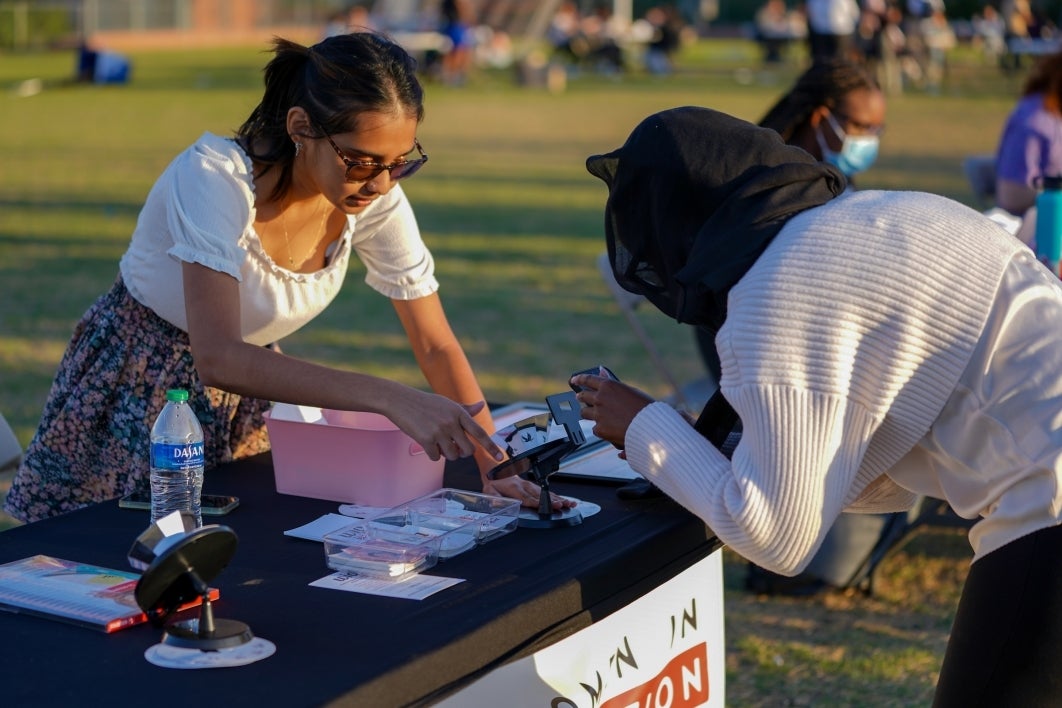 Woman spins a praxinoscope as another woman takes a video of it with her phone.