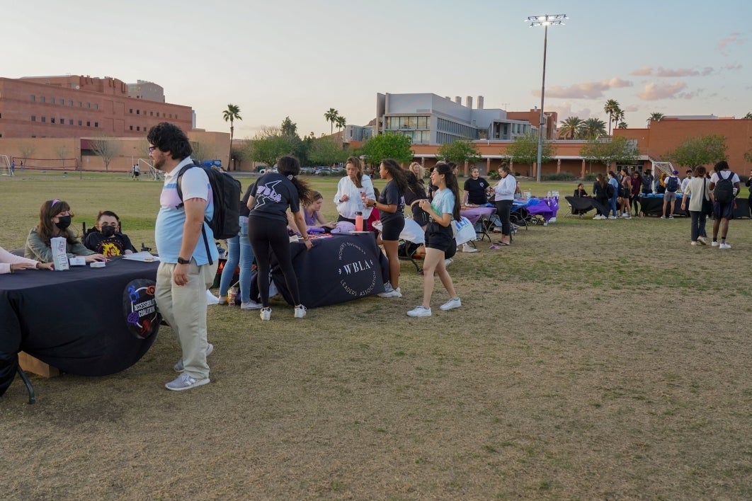 People standing and walking around a grassy field filled with tables.